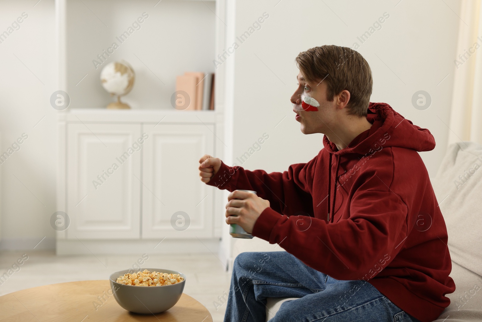 Emotional sports fan with drink and popcorn watching game at home Photo of Emotional sports fan with drink and popcorn watching game at home