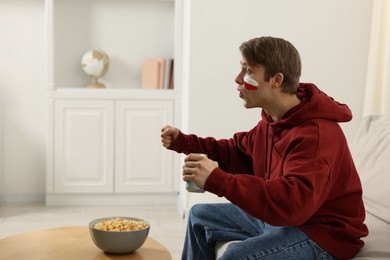 Photo of Emotional sports fan with drink and popcorn watching game at home