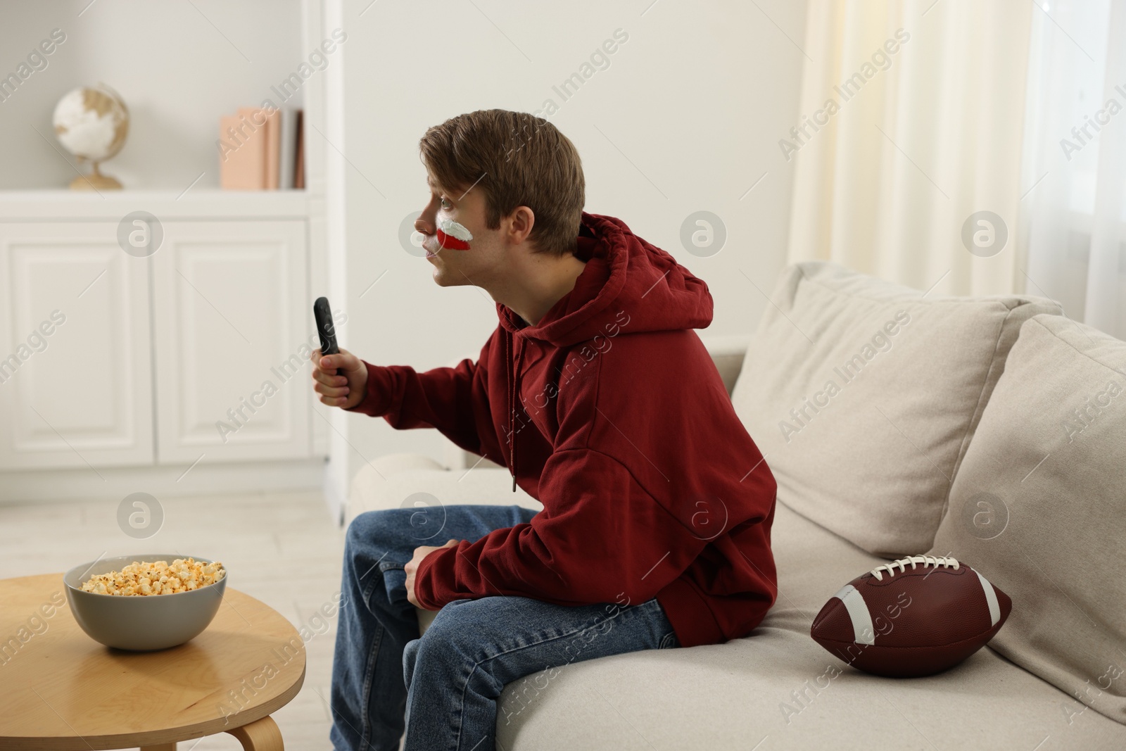 Emotional sports fan with remote control and ball watching game indoors Photo of Emotional sports fan with remote control and ball watching game indoors
