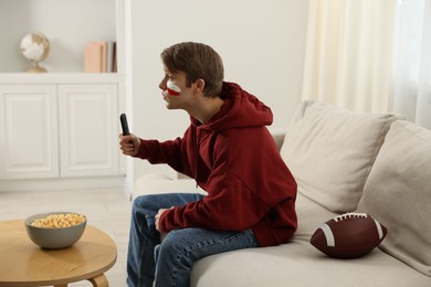 Photo of Emotional sports fan with remote control and ball watching game indoors