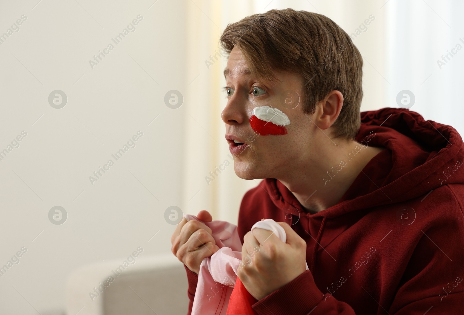 Emotional sports fan with flag of Poland watching game indoors, space for text Photo of Emotional sports fan with flag of Poland watching game indoors, space for text