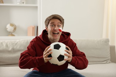 Photo of Emotional sports fan with soccer ball watching game indoors