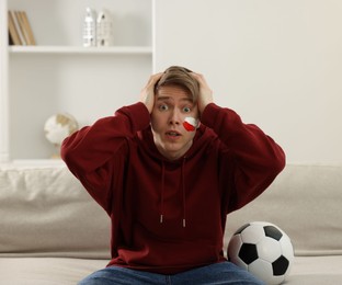 Photo of Emotional sports fan with soccer ball watching game indoors