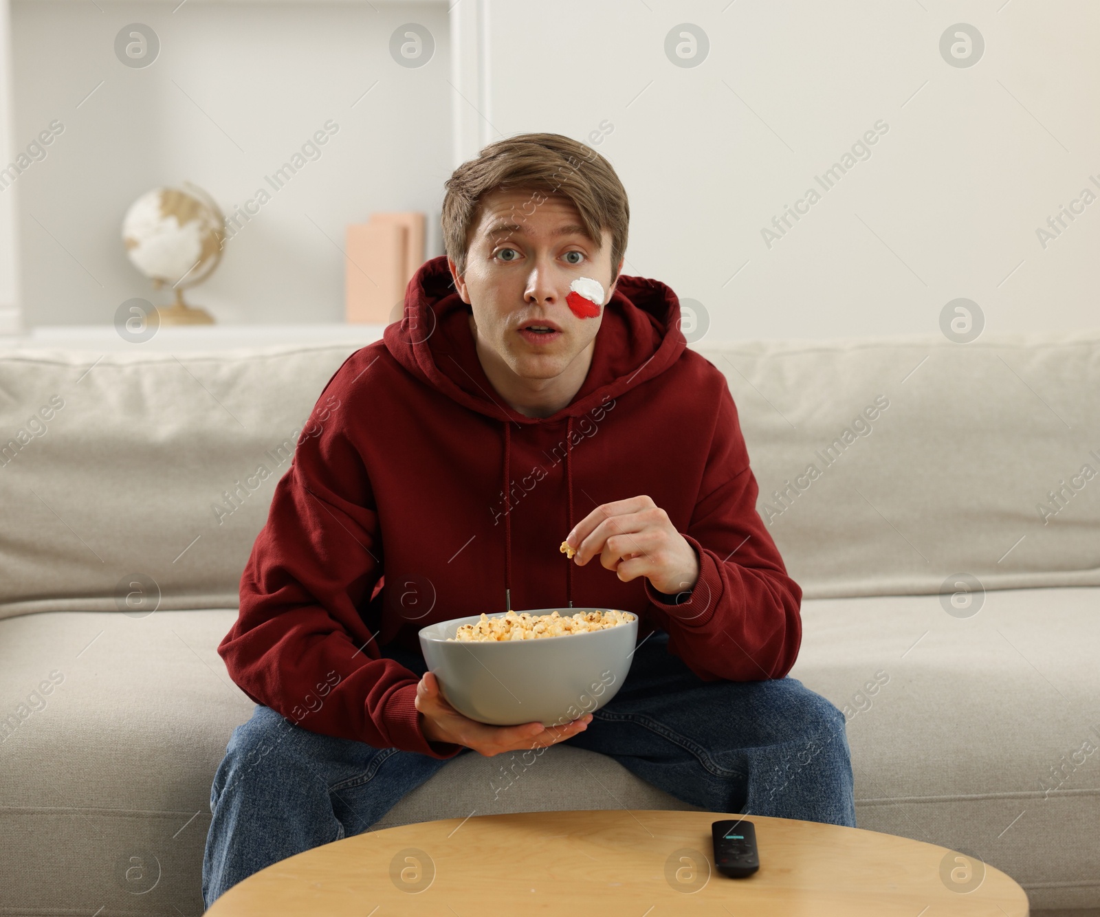 Sports fan eating popcorn while watching game on sofa indoors Photo of Sports fan eating popcorn while watching game on sofa indoors