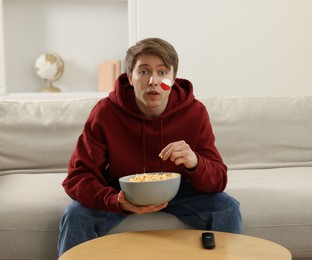 Photo of Sports fan eating popcorn while watching game on sofa indoors