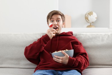 Photo of Sports fan eating popcorn while watching game on sofa indoors