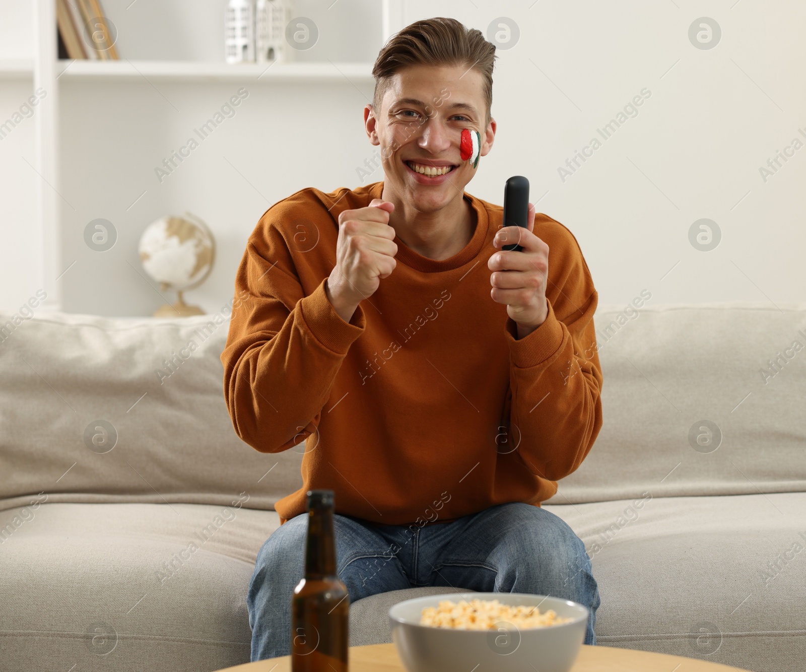 Sports fan with drawing of Italian flag and remote control watching game on sofa indoors Photo of Sports fan with drawing of Italian flag and remote control watching game on sofa indoors