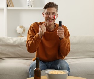 Photo of Sports fan with drawing of Italian flag and remote control watching game on sofa indoors