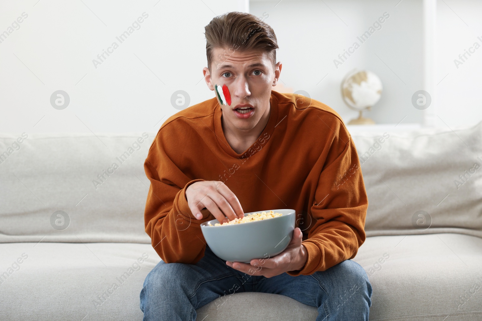 Sports fan eating popcorn while watching game on sofa indoors Photo of Sports fan eating popcorn while watching game on sofa indoors