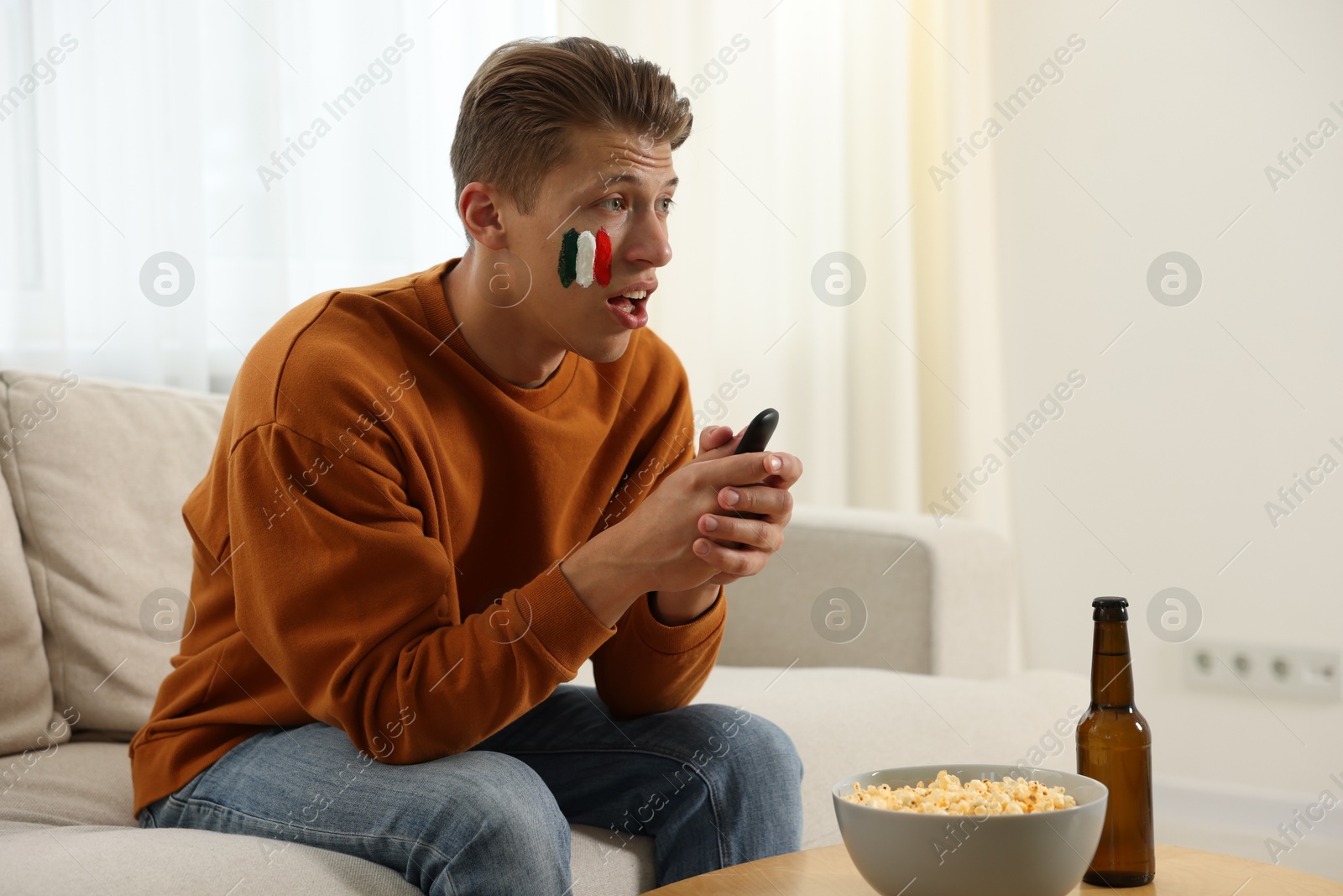 Sports fan with drawing of Italian flag and remote control watching game on sofa indoors Photo of Sports fan with drawing of Italian flag and remote control watching game on sofa indoors