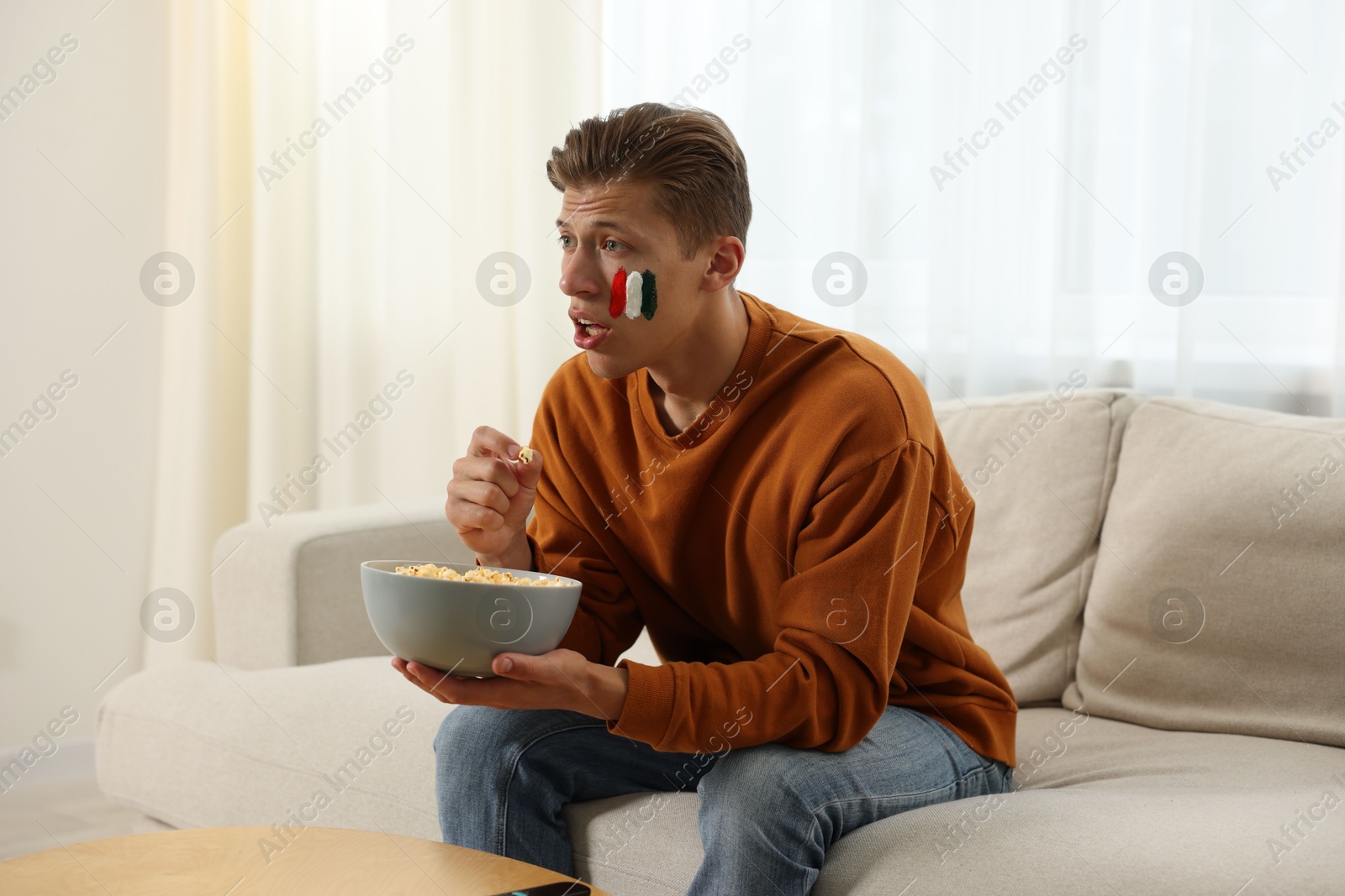 Sports fan eating popcorn while watching game on sofa indoors Photo of Sports fan eating popcorn while watching game on sofa indoors