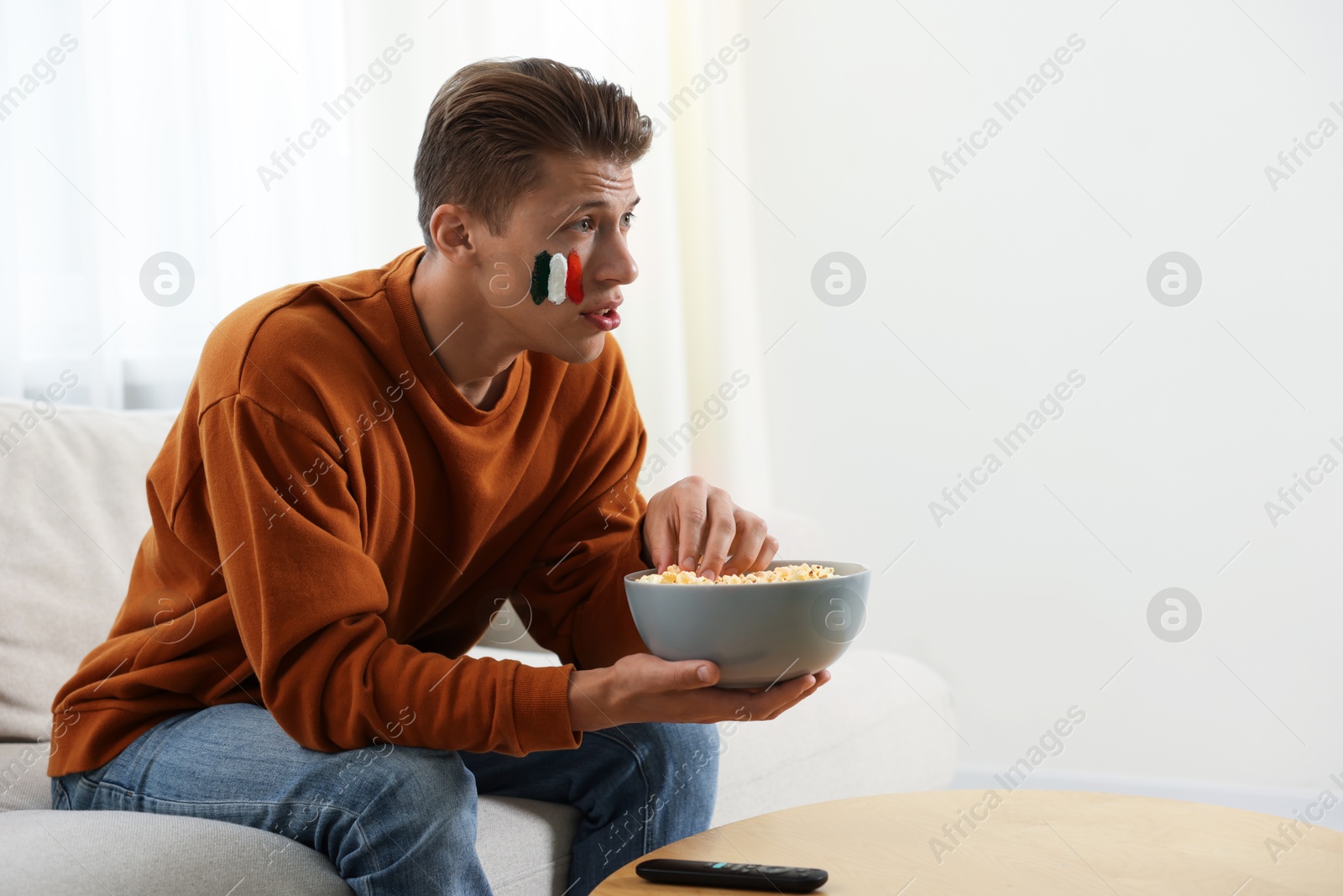 Sports fan eating popcorn while watching game on sofa indoors, space for text Photo of Sports fan eating popcorn while watching game on sofa indoors, space for text