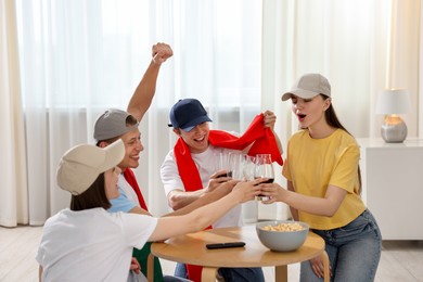 Photo of Emotional sports fans with drinks celebrating victory indoors