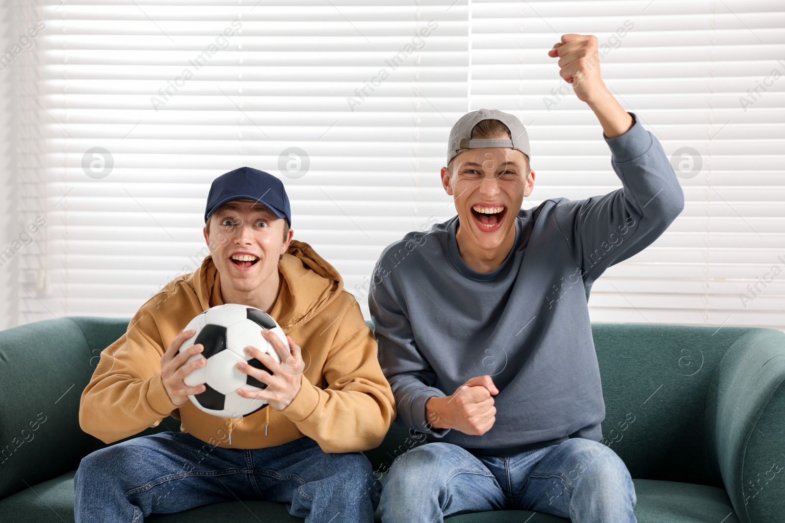 Emotional sports fans with soccer ball watching game together on sofa indoors Photo of Emotional sports fans with soccer ball watching game together on sofa indoors