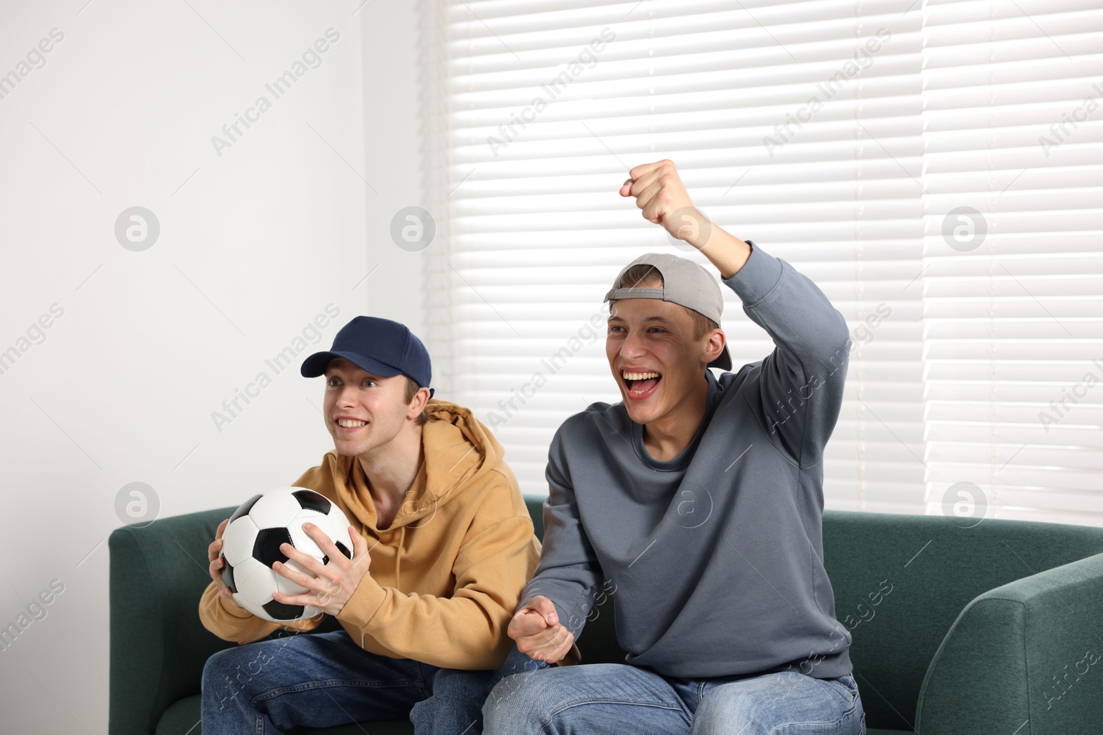 Emotional sports fans with soccer ball watching game together on sofa indoors Photo of Emotional sports fans with soccer ball watching game together on sofa indoors