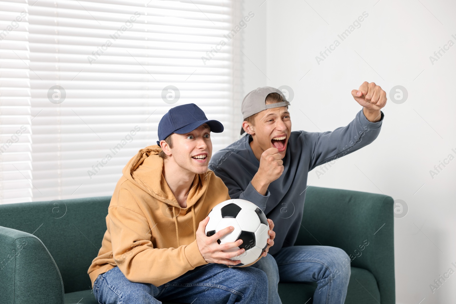 Emotional sports fans with soccer ball watching game together on sofa indoors Photo of Emotional sports fans with soccer ball watching game together on sofa indoors