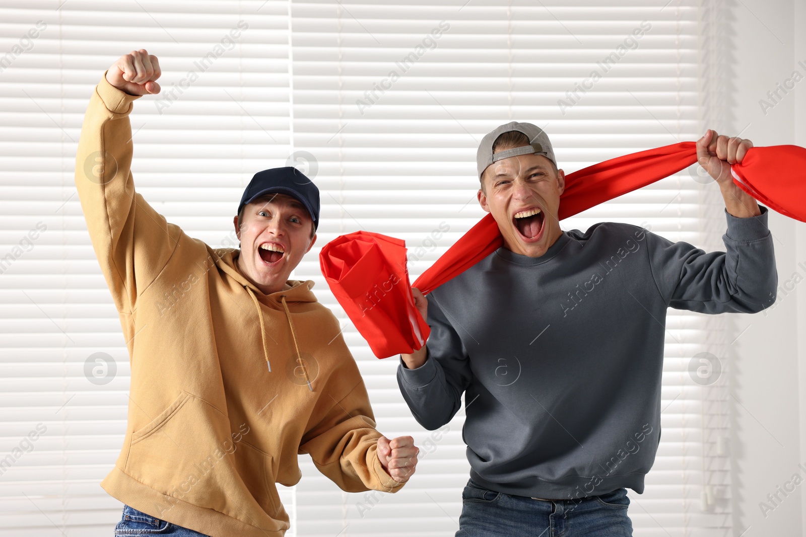 Emotional sports fans with flag near window indoors Photo of Emotional sports fans with flag near window indoors