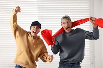 Photo of Emotional sports fans with flag near window indoors