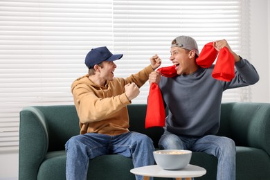 Photo of Emotional sports fans watching game together on sofa indoors