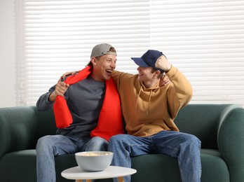 Photo of Emotional sports fans watching game together on sofa indoors
