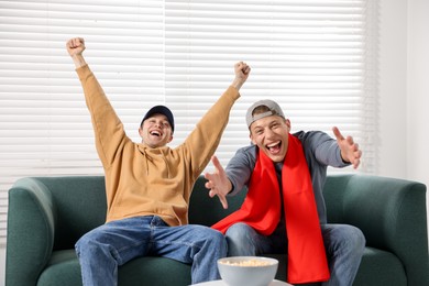 Photo of Emotional sports fans watching game together on sofa indoors