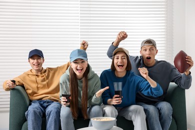 Photo of Emotional sports fans watching game together on sofa indoors