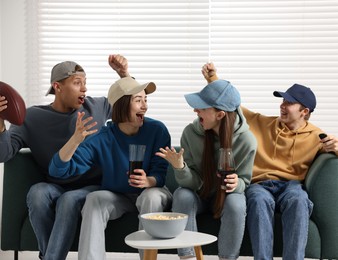 Photo of Emotional sports fans watching game together on sofa indoors