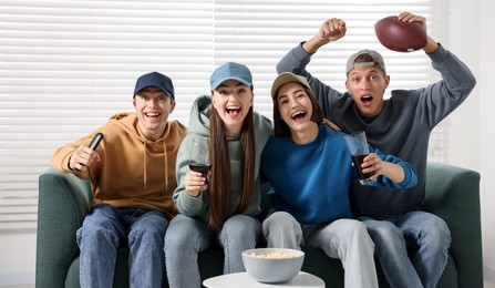 Photo of Emotional sports fans watching game together on sofa indoors