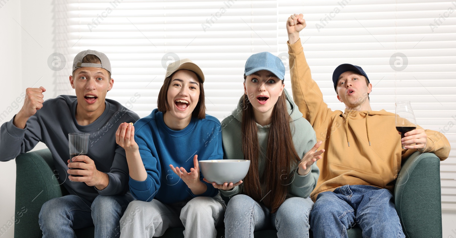 Emotional sports fans watching game together on sofa indoors Photo of Emotional sports fans watching game together on sofa indoors