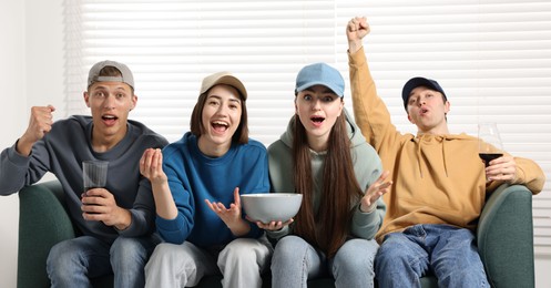Photo of Emotional sports fans watching game together on sofa indoors