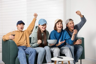 Photo of Emotional sports fans watching game together on sofa indoors