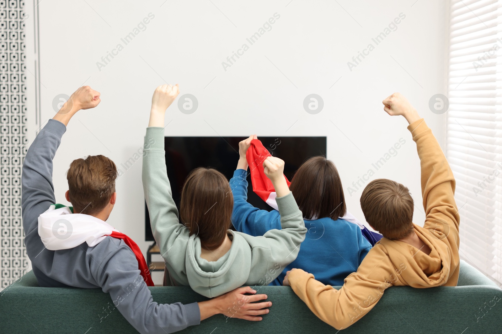 Emotional sports fans watching game together on sofa indoors, back view Photo of Emotional sports fans watching game together on sofa indoors, back view