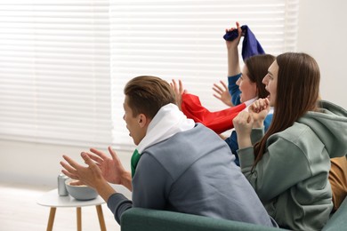 Photo of Emotional sports fans watching game together on sofa indoors