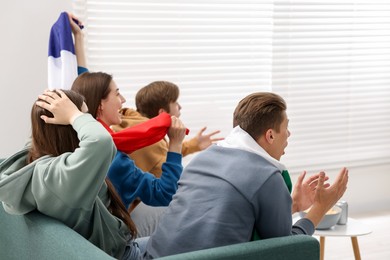 Photo of Emotional sports fans watching game together on sofa indoors