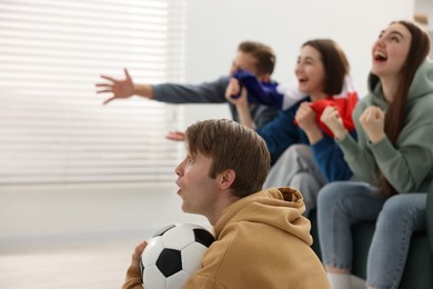 Photo of Emotional football fans watching game together indoors, selective focus. Space for text