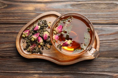 Photo of Aromatic herbal tea in glass cup, dry leaves and flowers on wooden table, top view