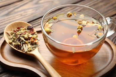 Photo of Aromatic herbal tea in glass cup and dry leaves on wooden table, closeup