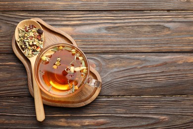 Photo of Aromatic herbal tea in glass cup and dry leaves on wooden table, top view. Space for text