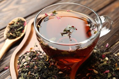 Photo of Aromatic herbal tea in glass cup and dry leaves on wooden table, closeup