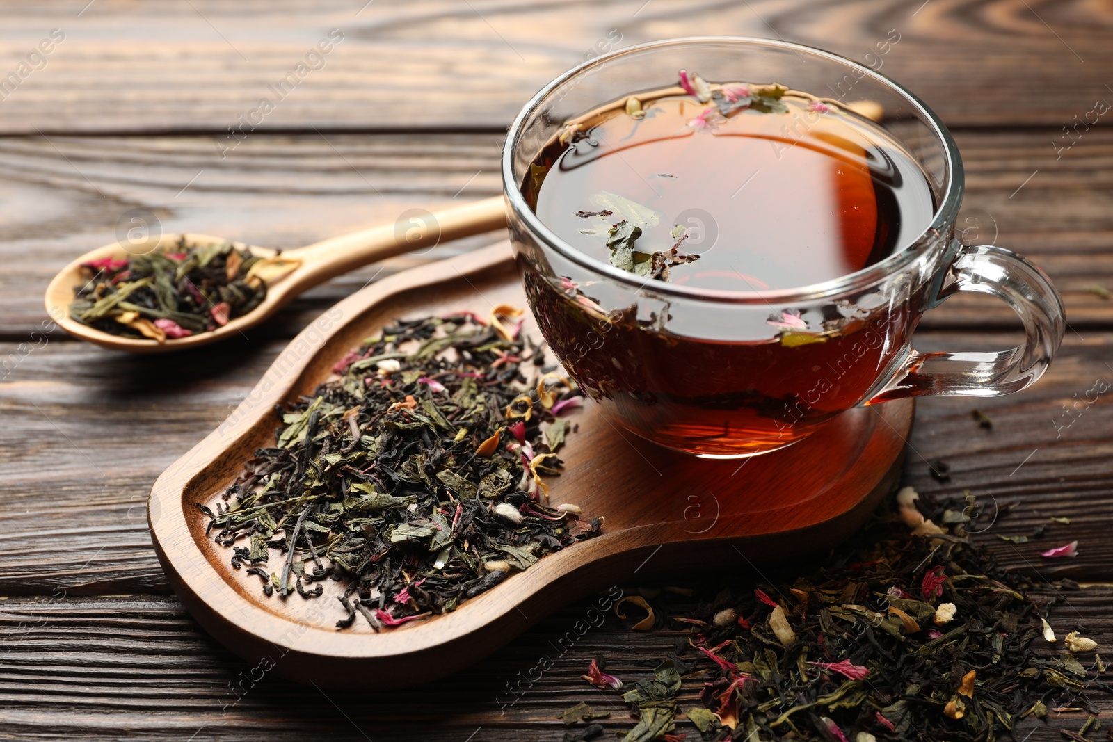 Aromatic herbal tea in glass cup and dry leaves on wooden table, closeup Photo of Aromatic herbal tea in glass cup and dry leaves on wooden table, closeup