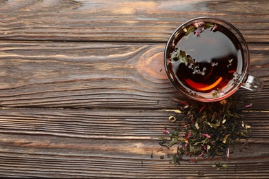 Photo of Aromatic herbal tea in glass cup and dry leaves on wooden table, flat lay. Space for text