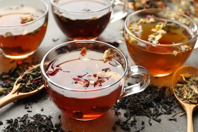Photo of Aromatic herbal tea in glass cups and dry leaves on grey table, closeup