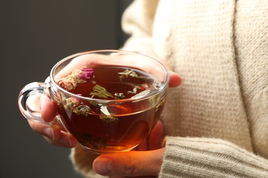 Photo of Woman with glass cup of aromatic herbal tea on grey background, closeup