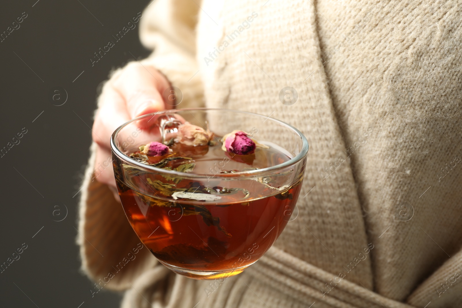 Woman with glass cup of aromatic herbal tea on grey background, closeup Photo of Woman with glass cup of aromatic herbal tea on grey background, closeup