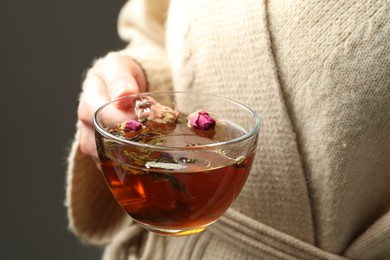 Photo of Woman with glass cup of aromatic herbal tea on grey background, closeup