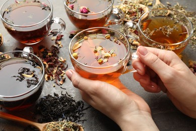 Photo of Woman with aromatic herbal tea, dry leaves and flowers at grey table, closeup
