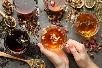Photo of Woman with aromatic herbal tea, dry leaves and flowers at grey table, top view