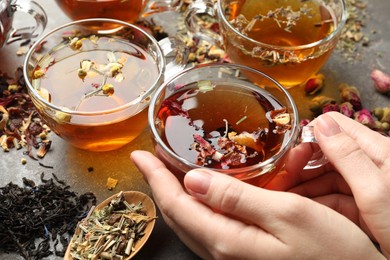 Photo of Woman with aromatic herbal tea, dry leaves and flowers at grey table, closeup