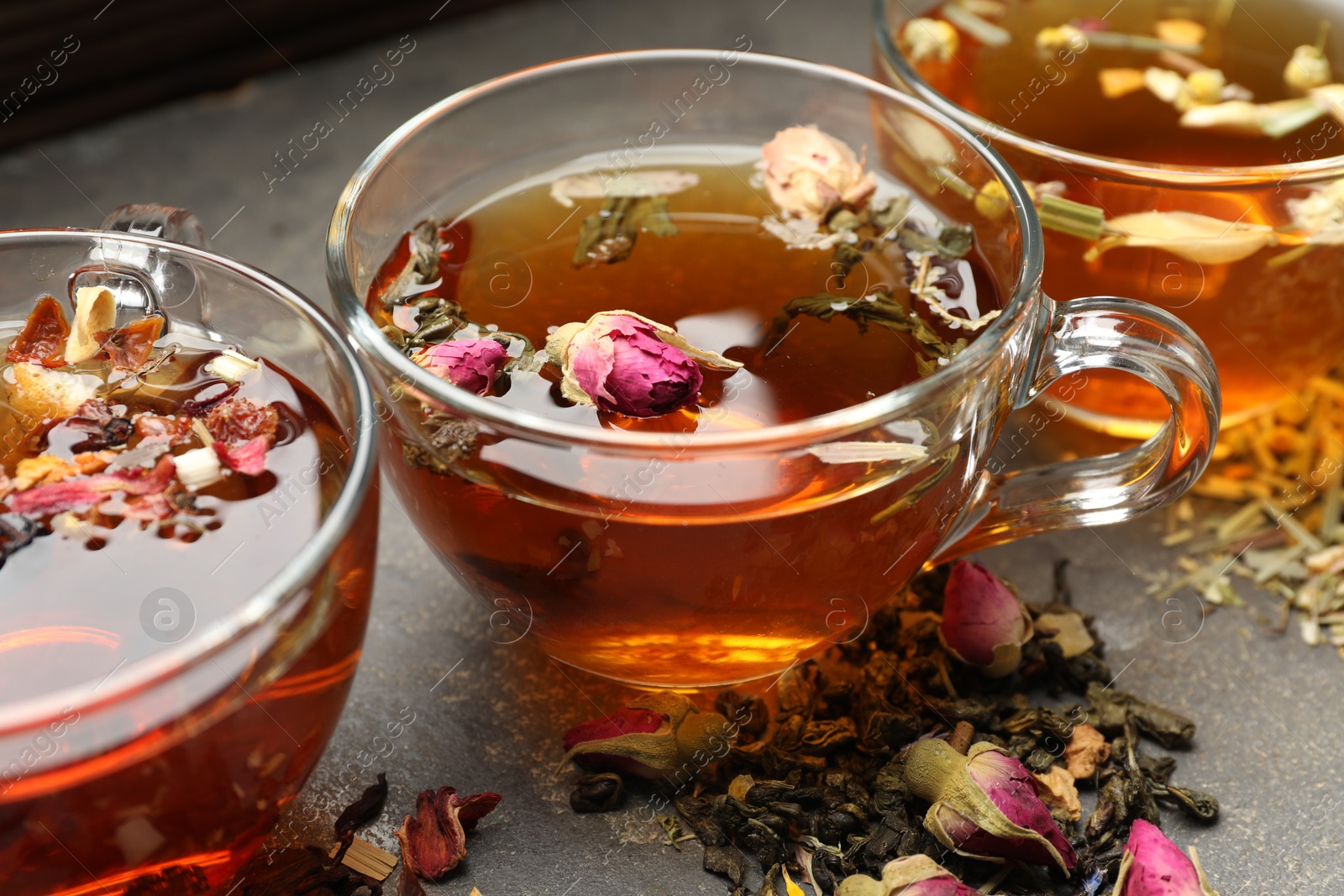 Aromatic herbal tea in glass cups, dry leaves and flowers on grey table, closeup Photo of Aromatic herbal tea in glass cups, dry leaves and flowers on grey table, closeup