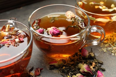 Photo of Aromatic herbal tea in glass cups, dry leaves and flowers on grey table, closeup
